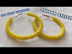 two yellow beaded hoop earrings sitting on top of a white cloth covered table with the words diy hoop earrings ladder stitch