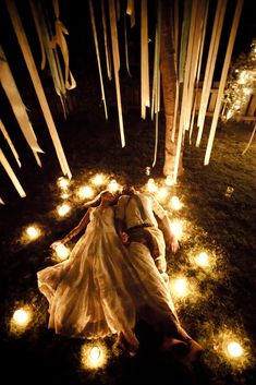 a person laying on the ground surrounded by candles and trees with lights in the grass