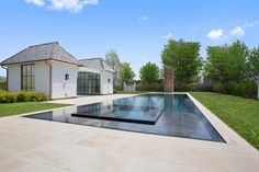 an empty swimming pool in front of a white house with green grass and trees around it