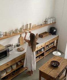 a woman standing in a kitchen next to a counter with plates and bowls on it