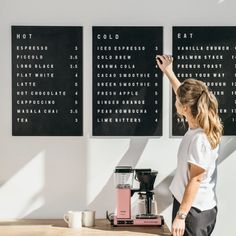 a woman standing at a counter in front of a coffee machine and menus on the wall