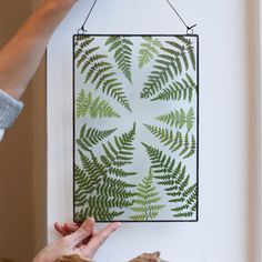 a woman is hanging a green fern leaf art piece on the wall with her hands