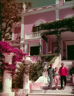 two people standing on steps in front of a pink house