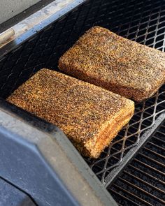 two pieces of meat cooking on top of a grill with grated bread and seasoning