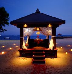 a gazebo on the beach with lit candles around it