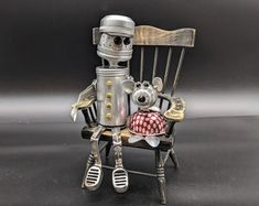 a metal robot sitting on top of a wooden chair with a red and white checkered pillow