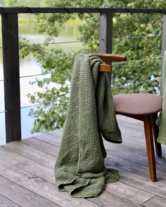 a green blanket sitting on top of a wooden deck next to a chair and tree