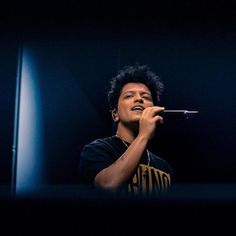 a young man holding a microphone up to his mouth while singing into a mic in the dark