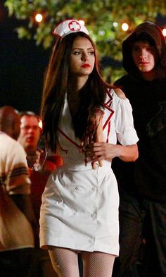 a woman dressed in white walking down the street with a man behind her wearing a red and white hat