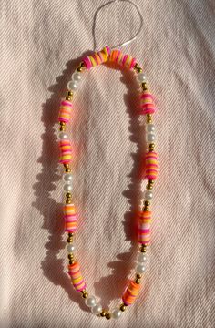 a beaded necklace with beads and gold accents on a white surface, next to a pair of scissors