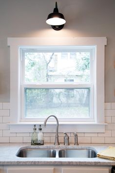 a kitchen sink under a window in front of a white tiled wall and counter top