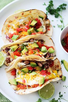 three tacos on a plate with salsa and avocado next to the tortilla