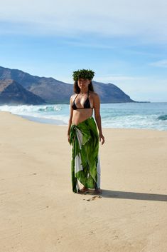 a woman standing on top of a sandy beach next to the ocean wearing a green skirt