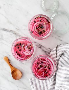 three glasses filled with food sitting on top of a marble counter next to a wooden spoon