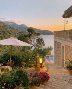 an outdoor patio with umbrellas and potted plants next to the water at sunset