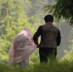 a man and woman are walking through the woods with their covers over their backs as they hold hands