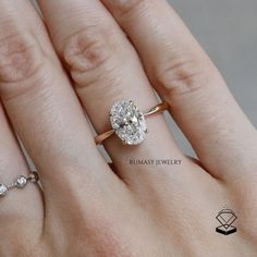 a woman's hand with two engagement rings on top of her finger and the ring has an oval diamond in it