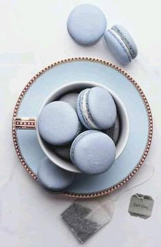 some blue macaroons are in a bowl on a white tablecloth with silver trim