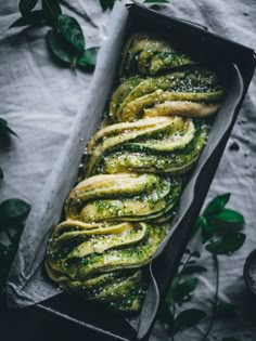 green pesto pasta in a black box on top of a white tablecloth with leaves