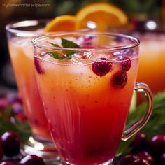 two glasses filled with drinks sitting on top of a table next to oranges and cranberries