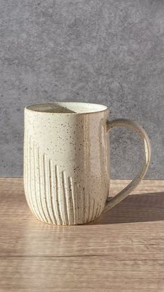 a white coffee cup sitting on top of a wooden table next to a gray wall