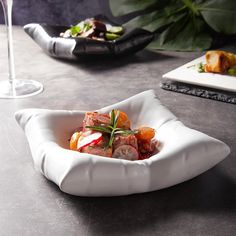 a white bowl filled with food on top of a table next to a glass of wine