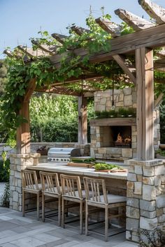 an outdoor kitchen with grill and table surrounded by greenery on the outside patio area