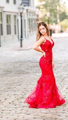 a woman in a red dress standing on a cobblestone street with her hands on her hips