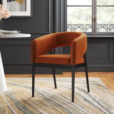 an orange chair sitting on top of a rug in front of a table with flowers