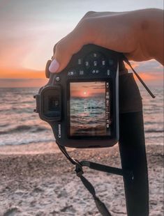 a person holding up a camera to take a photo on the beach at sunset or sunrise