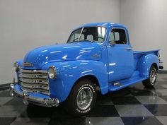 an old blue truck is parked on a checkered floor