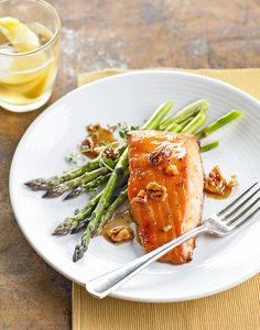 a white plate topped with salmon and asparagus next to a glass of lemonade