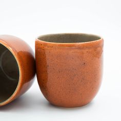 a brown cup sitting on top of a white table next to a ceramic container with a black lid