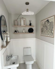 a white toilet sitting in a bathroom next to a sink under a framed art piece