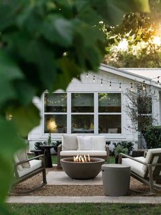 a fire pit sitting in the middle of a yard next to chairs and tables with lights on them