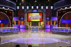 an empty stage with several people sitting at it and two television screens on the wall