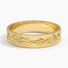 a yellow gold wedding band with mountains in the background and waves on it's surface