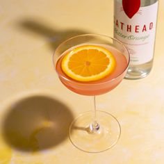 an orange slice in a martini glass next to a bottle