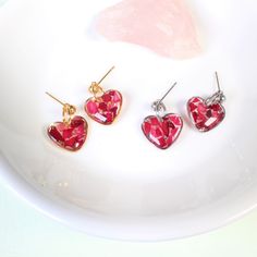 three pairs of heart shaped earrings sitting on top of a white plate next to a pink stone