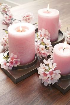 three pink candles sitting on top of each other next to some white and pink flowers