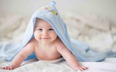 a baby laying on top of a bed under a blue towel and smiling at the camera