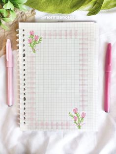 a notepad with pink flowers on it next to a pen and flower potted plant