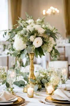 a tall vase with white flowers and greenery sits on top of a dining table