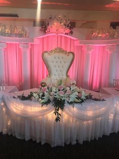 a fancy chair with flowers and greenery on the table in front of pink drapes