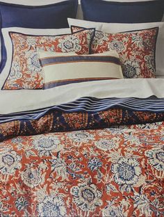 a bed with an orange and blue bedspread, pillows and blankets on it