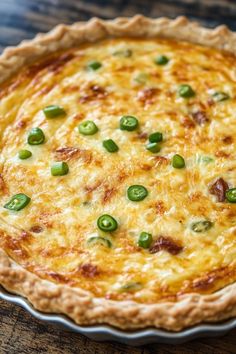 a cheesy quiche with green onions and cheese in a pie pan on a wooden table