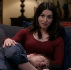 a woman laying on top of a couch next to a man in a red shirt