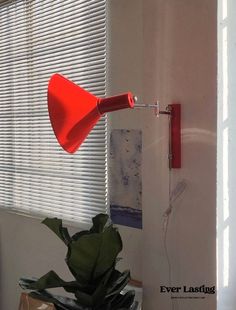 a red light is hanging from the side of a wall next to a potted plant