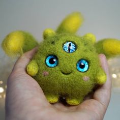 a hand holding a green stuffed animal with blue eyes