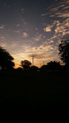 the sun is setting behind power lines and telephone poles in an open field with trees